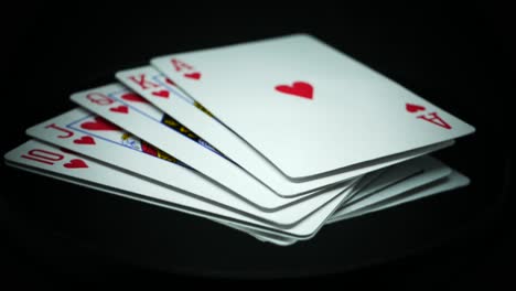 Royal-Flush-Aus-Herzen,-Die-Auf-Einer-Reflektierenden-Oberfläche-Vor-Schwarzem-Hintergrund-Rotieren-–-Nahaufnahme,-Studioaufnahme