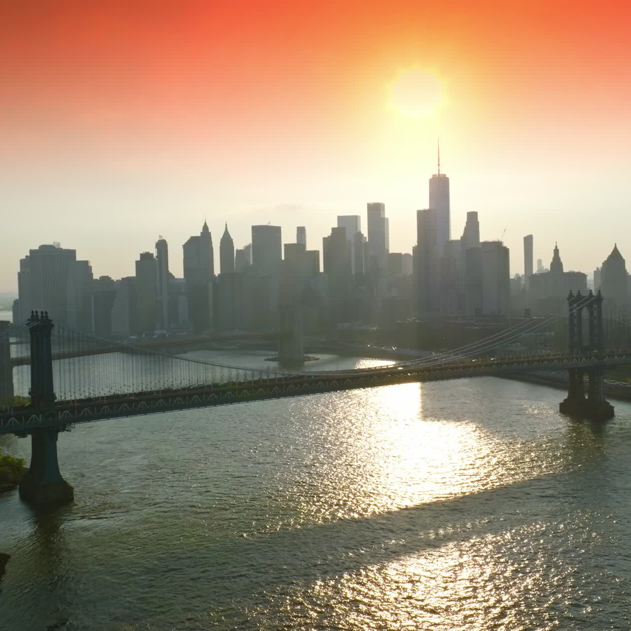 Setting sun over the grey silhouettes of New York skyscrapers. Beautiful bridges over the East River at backdrop of pink sky