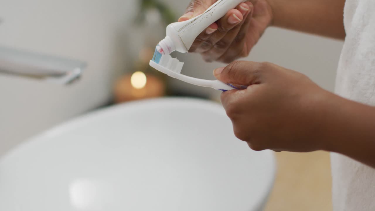 sección media de una mujer afroamericana cepillándose los dientes en el baño