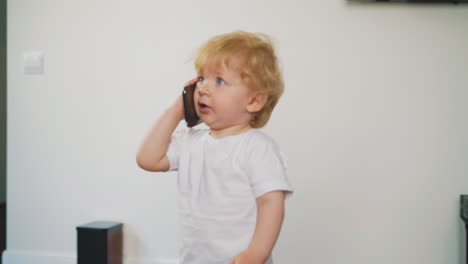 little child in white t-shirt and bloomers walks with phone