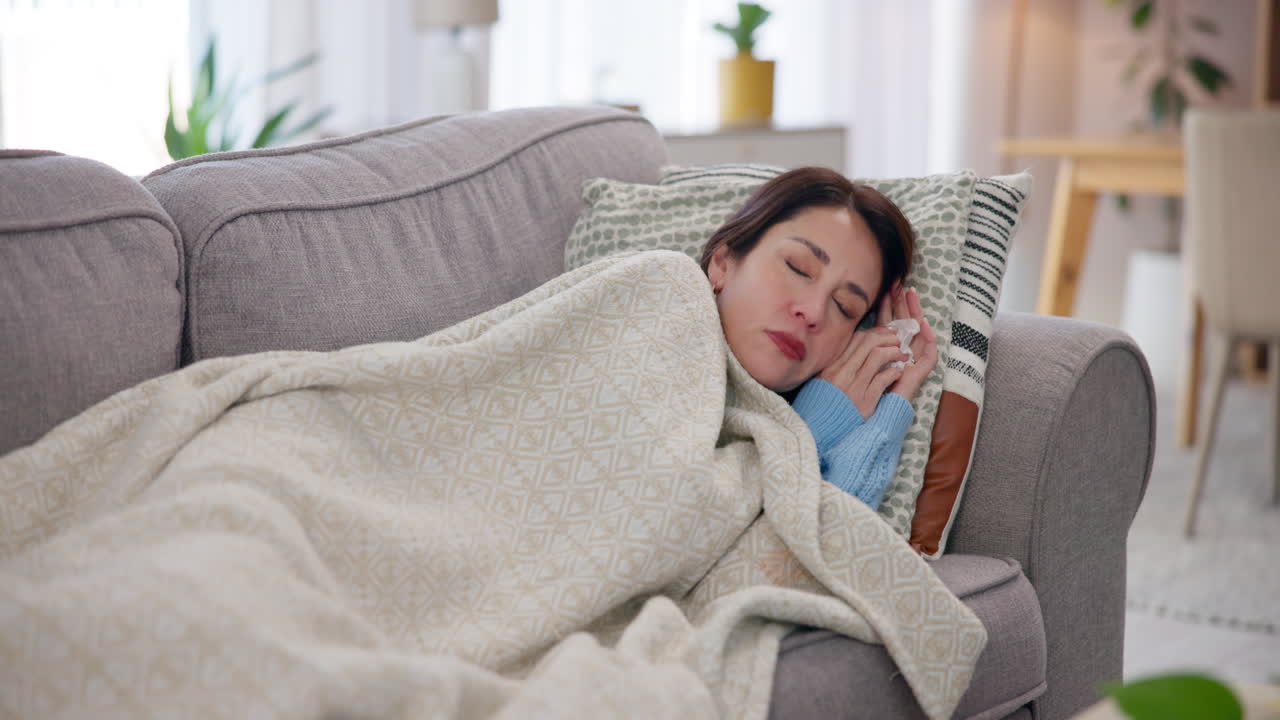 A woman is sick and sleeping on a couch under a blanket.