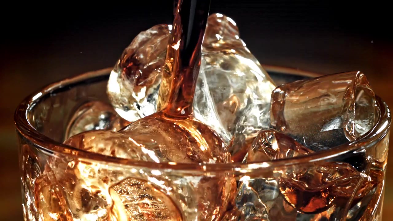 Liquido scuro versato su cubetti di ghiaccio in un bicchiere al rallentatore