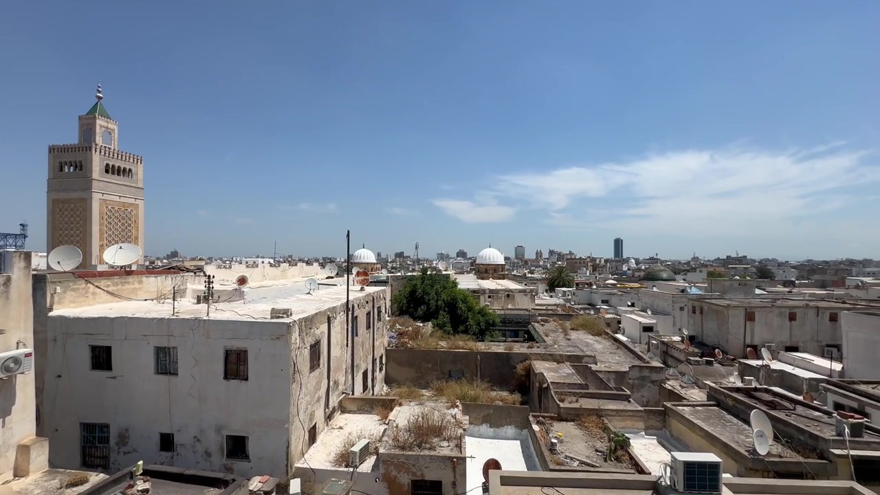 Tetti tradizionali della medina di Tunisi e antenne paraboliche incorniciano un minareto di moschea sotto un cielo azzurro brillante a Tunisi, Tunisia.