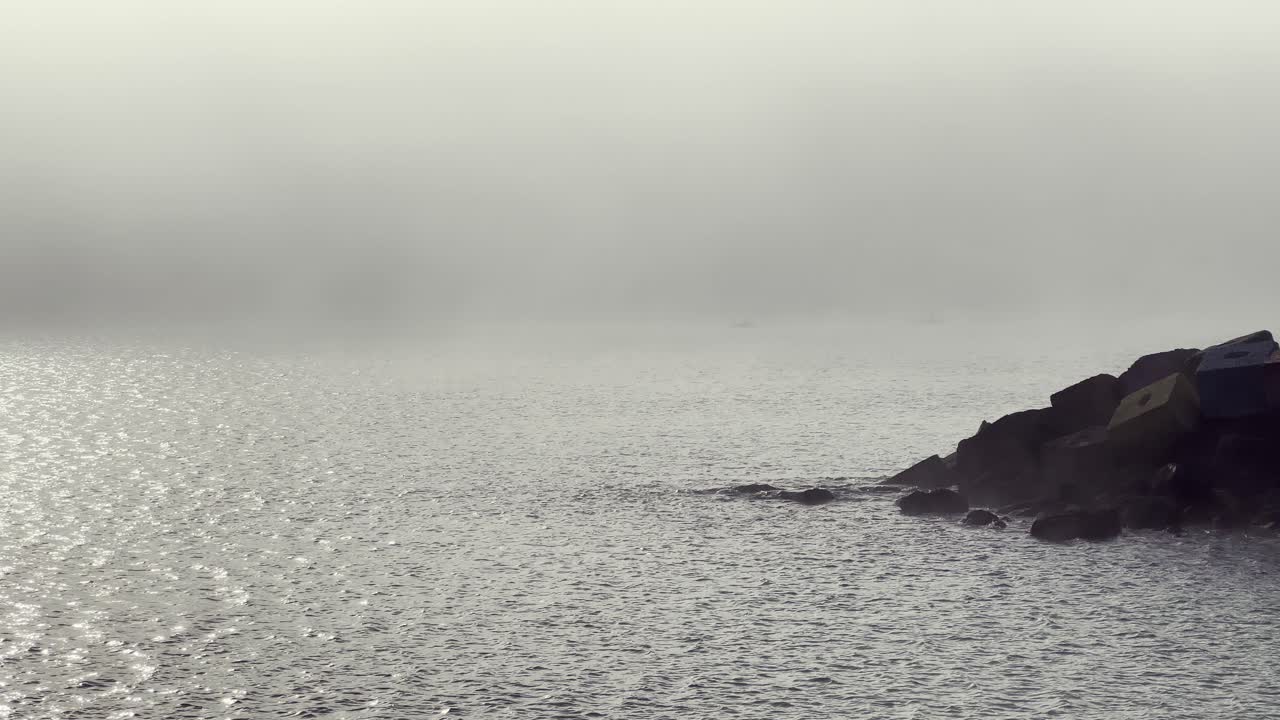 Fog rolling over the Atlantic Ocean from a rocky Barbate coast during a cloudy day creates a melancholic and serene seascape, enveloping the landscape in a tranquil mood