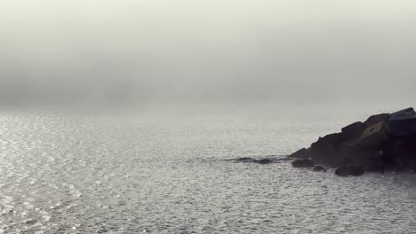 fog rolling over the atlantic ocean from a rocky barbate coast during a cloudy day creates a melancholic and serene seascape, enveloping the landscape in a tranquil mood