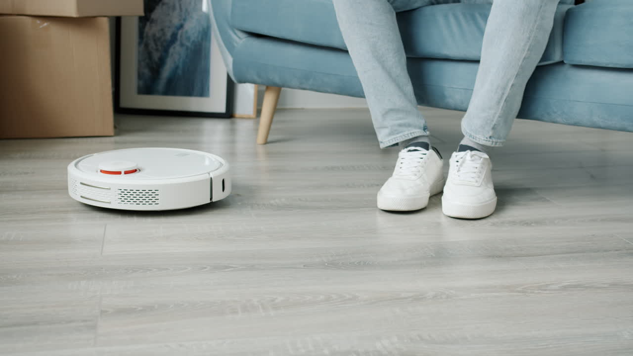 Robot Vacuum Cleaning a Floor with Person Sitting on a Sofa