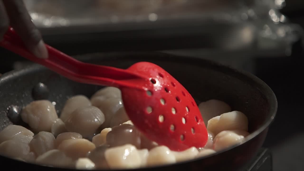 Scallops being prepared on the in a frying pan with some stirring.