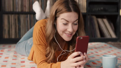 Hermosa-Mujer-En-Casa-Hablando-Con-Un-Amigo-En-Una-Aplicación-De-Teléfono-Inteligente-En-Un-Dispositivo-Portátil-Tumbado-En-El-Suelo-Relajado-Tomando-Café