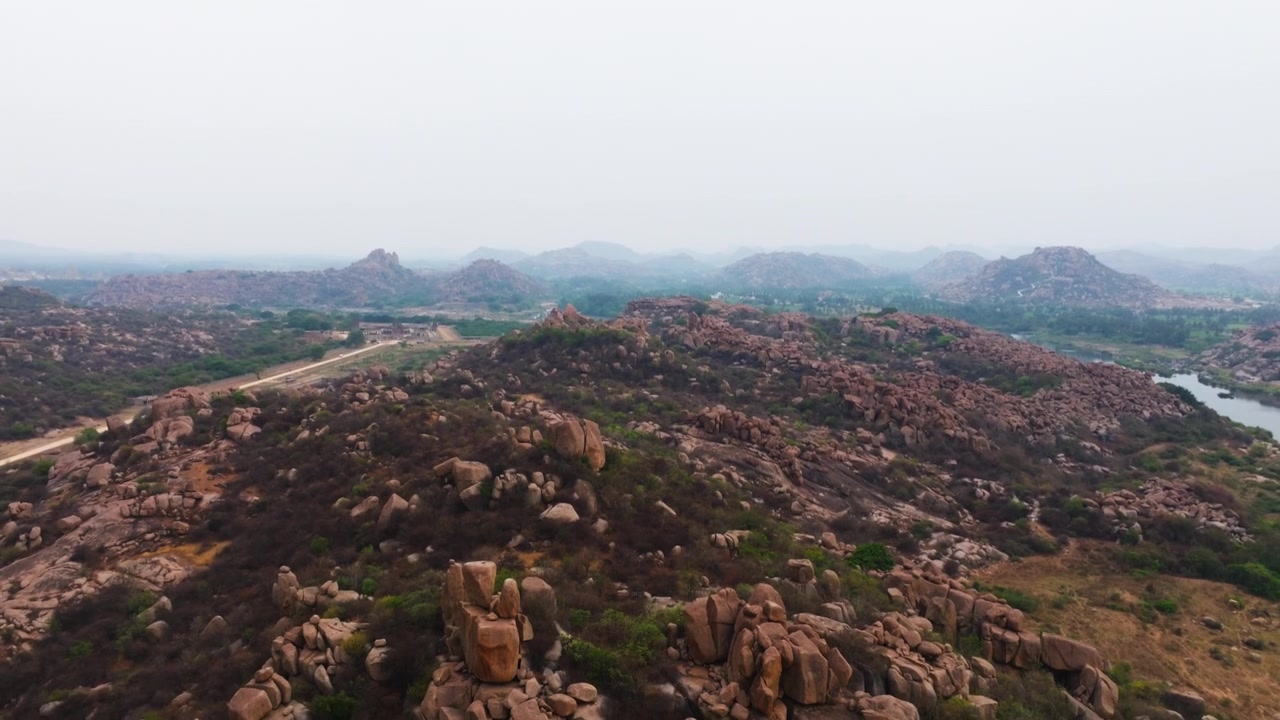 Steinete terreng med Sahyadri-fjellene, Tungabhadra-elven og Vitthal Mandirv i Nimbapura, Hampi, Karnataka, India. Dagtid, kranbilde, dronebilde, 4k