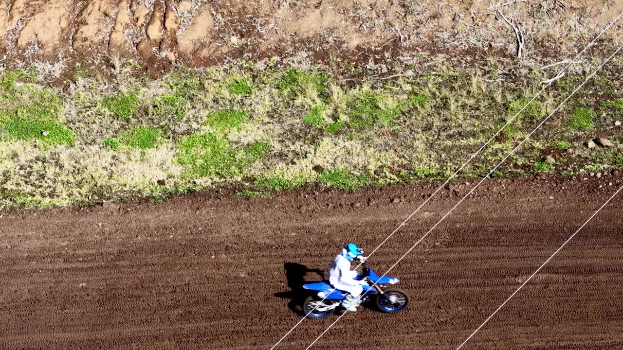 Tomada de drone em ângulo elevado de um piloto de motocross correndo por uma pista de terra rural.