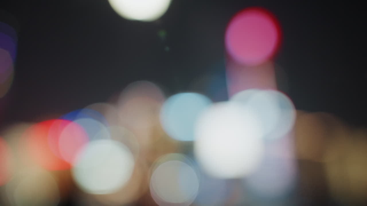 Luci sfocate della città di notte con effetto bokeh, morbida luce cinematografica con riflessi al neon e forme di lampade fuori fuoco, palette di colori suggestiva, grana sottile e profondità di campo ridotta creano un astratto urbano atmosferico.