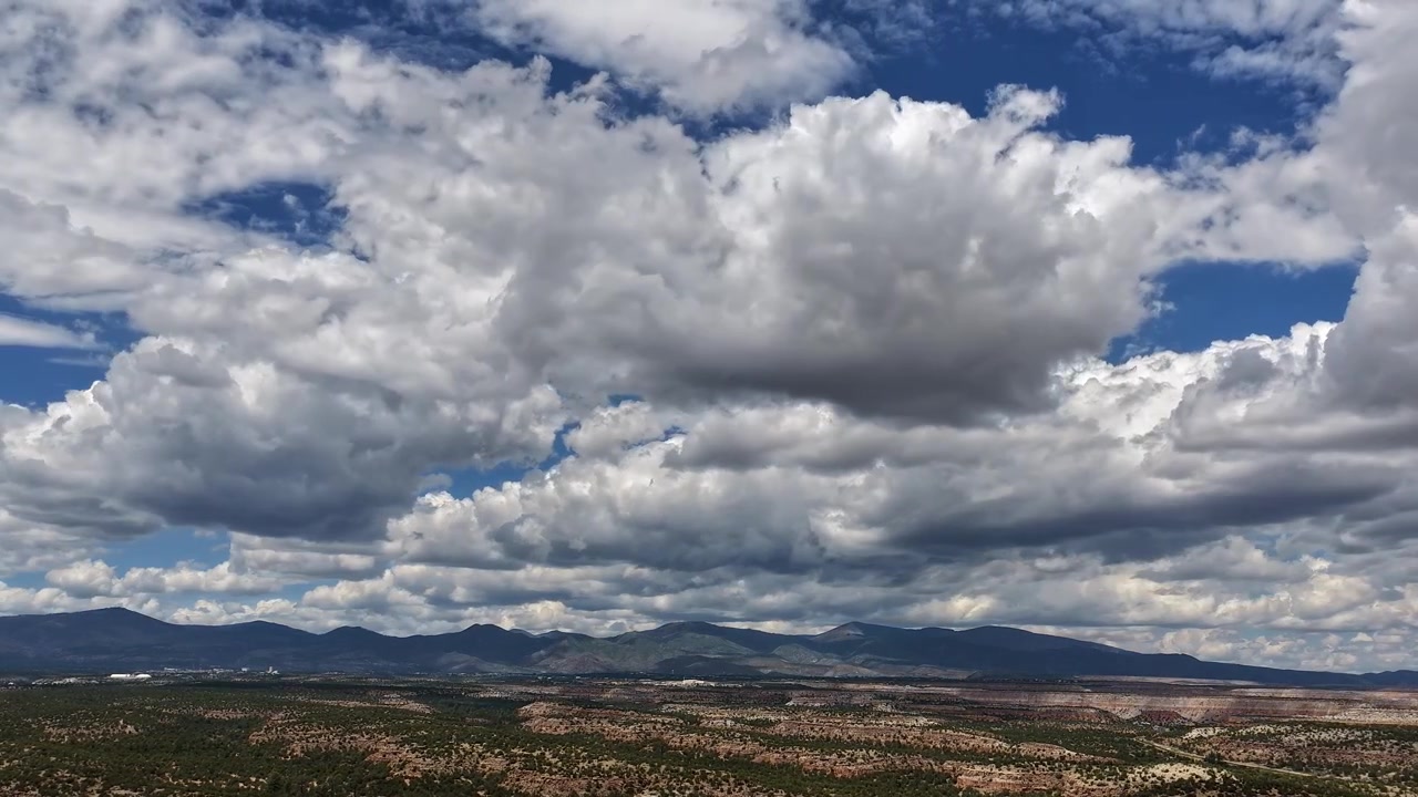 Timelapse 4K con drone che cattura enormi nuvole cumuliformi che si muovono su un vasto e arido paesaggio di mesa nel Nuovo Messico. Ombre dense di nuvole si estendono sull'altopiano profondo verso le lontane montagne Jemez.