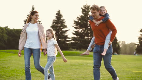 pais felizes com suas duas filhas caminhando juntos no parque