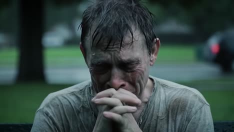 a man sits alone on a park bench, drenched by heavy rain. he is visibly upset, with tears streaming down his face as he appears to be lost in thought.