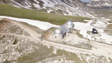 Wide-angle-drone-shot-panning-upwards-of-a-busy-observatory-with-hikers-walking-by-revealing-the-mountain-landscape-in-the-distance-in-the-region-of-Abruzzo-in-Italy