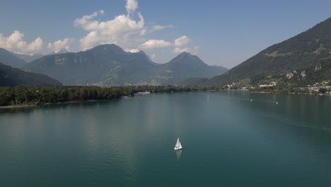 orbit movement around white sailing boat staying still anchored in the middle of an amazing lake creating reflections in the water nearby town built along the shore small community adventure trip