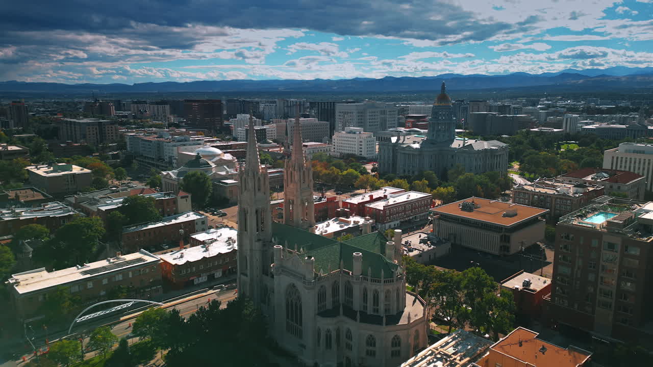 Approaching the beautiful building of the Cathedral Basilica of the Immaculate Conception. State Capitol Building in Denver, Colorado, USA at backdrop. Fluffy clouds cover the sky over the city