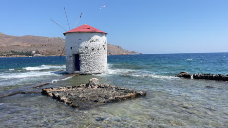 greece,leros island,famous windmill in the sea at agia marina. white waves hit the windmill and surfs occur. a seagull flies and lands on the windmill.