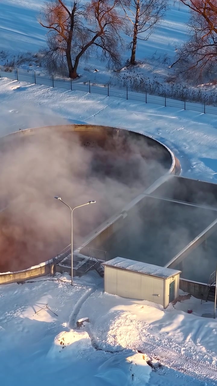 Vertikalt droneoptagelse af et industrielt vandbehandlingsanlæg dækket af sne om vinteren, der viser frossen infrastruktur, kold atmosfære og essentielle bymæssige vandforvaltningssystemer