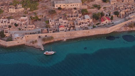 Ausflugsboot-Navigiert-Entlang-Des-äußeren-Randes-Der-Festungsruinen-Von-Spinalonga,-Während-Eine-Strukturierte-Wasserströmung-Die-Insel-Erreicht