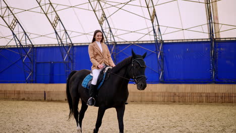 woman riding a black horse in an indoor riding arena