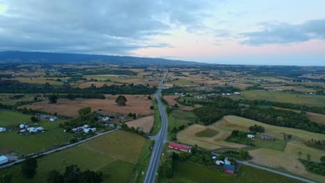 Chiloé,-Chile-In-Der-Abenddämmerung-Mit-Einer-Kurvenreichen-Straße-Inmitten-Grüner-Felder-Und-Verstreuter-Häuser,-Luftaufnahme