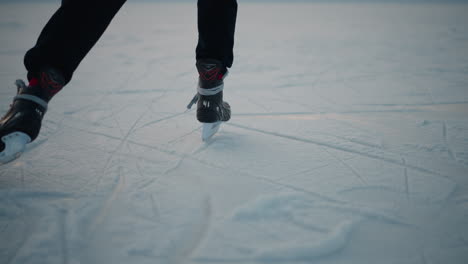 lower angle view of skater skillfully gliding across ice rink in winter park with textured ice surface and blurred background of other skaters and urban buildings under soft daylight