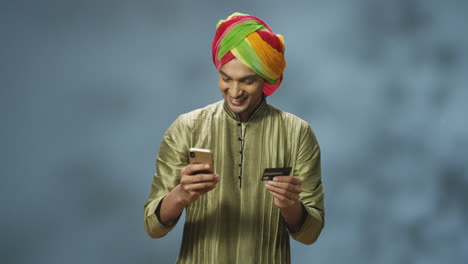 handsome joyful indian man in turban and traditional clothes shopping online with smartphone, then he laughs and celebrates