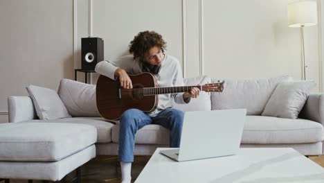 young man learning guitar online at home