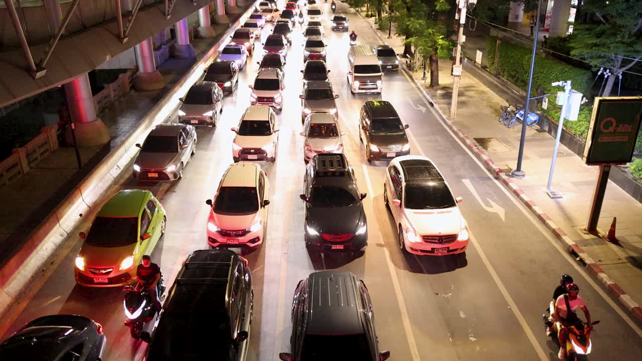 Overhead view of congested city street with cars, motorcycles, and bright urban night lighting
