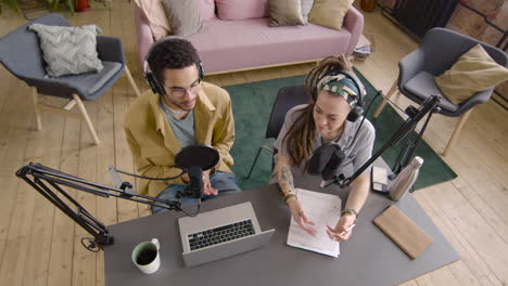 vista superior de un hombre y una mujer jóvenes con auriculares sentados en una mesa con micrófonos mientras graban un podcast 3