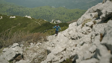 hiker climbing on a rocky path towards the peak of mountain snežnik, helping himself with hiking poles with balance