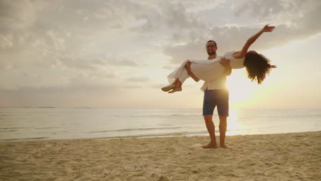 el esposo rodea a su esposa en sus brazos contra el fondo del mar y la puesta de sol feliz luna de miel