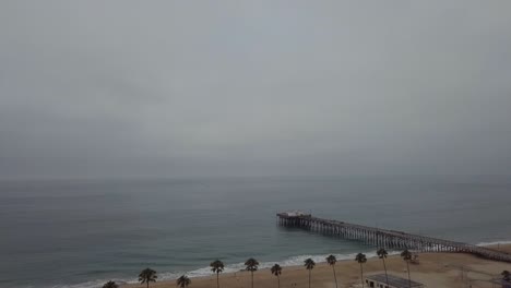 vista del muelle y del océano pacífico detrás de las palmeras en una mañana gris y fría