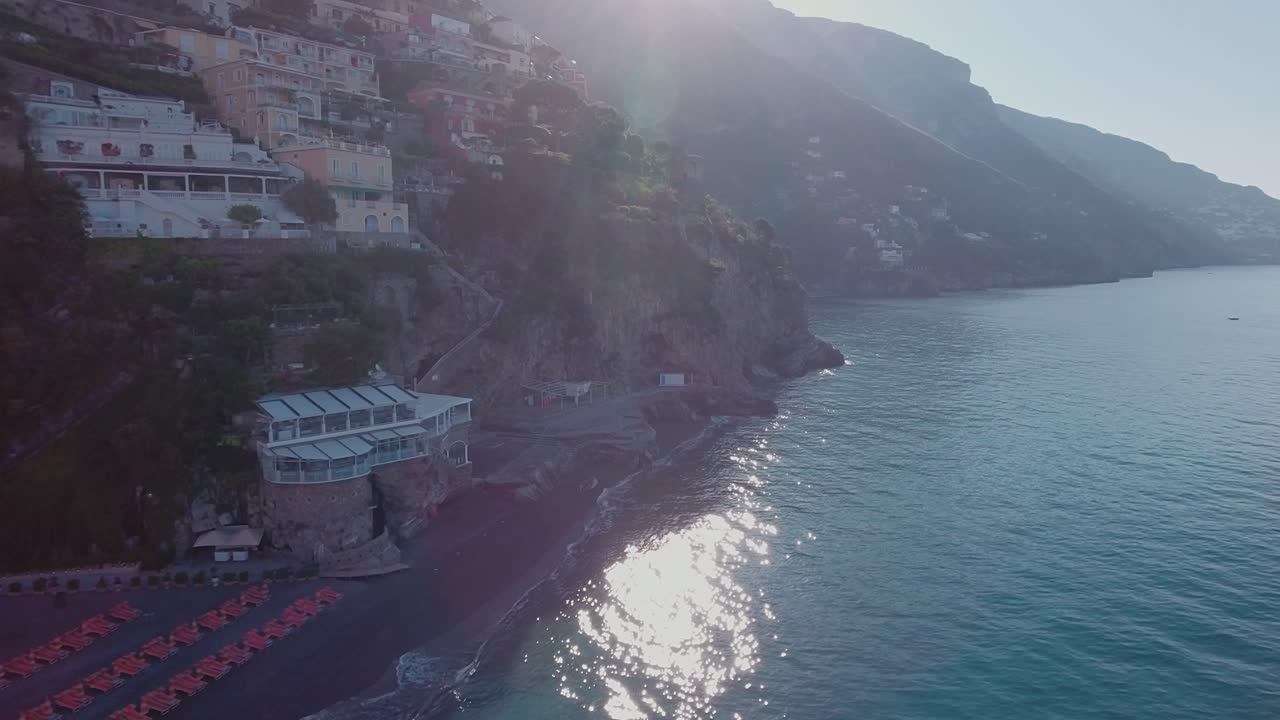 Ripresa aerea con drone in volo verso la spiaggia a Positano, Italia, a bassa quota con bagliore dell'obiettivo.