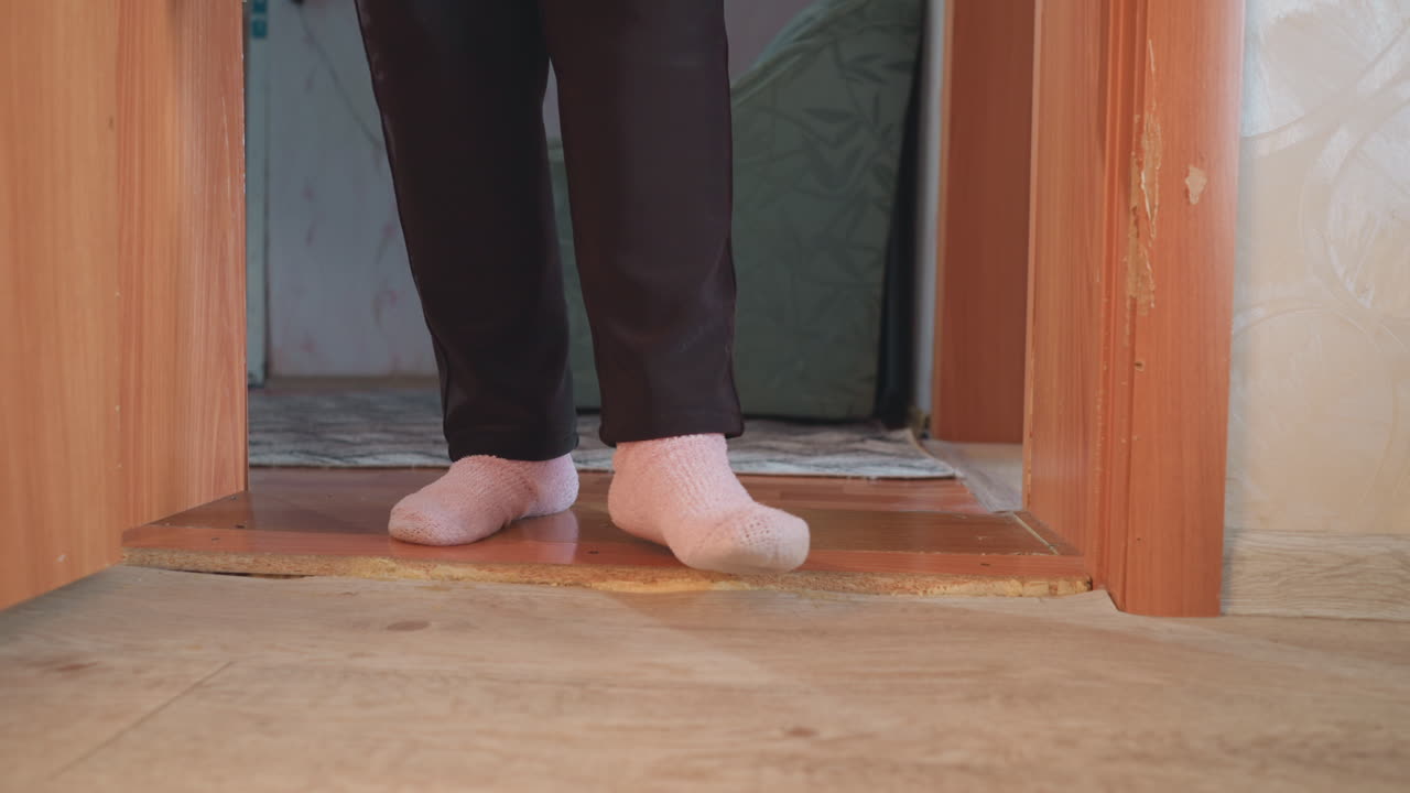Close-up of elderly woman s feet in pink socks walking on wooden floor, relaxed indoor atmosphere, soft lighting from nearby window, peaceful home environment with minimalistic decor and warm tones