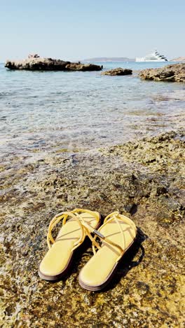 stylish yellow sandals resting on rocks by clear blue sea