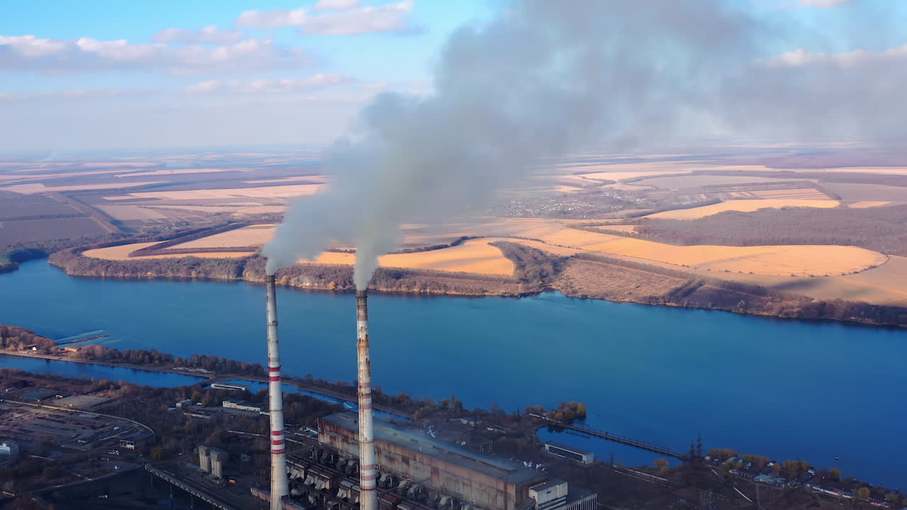 View from the drone at the old aged weathered tall industrial factory chimney with smoke over it. Cloudy sky background