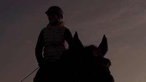 beautiful silhouette rider mounted on grazing horse at sunset, medium