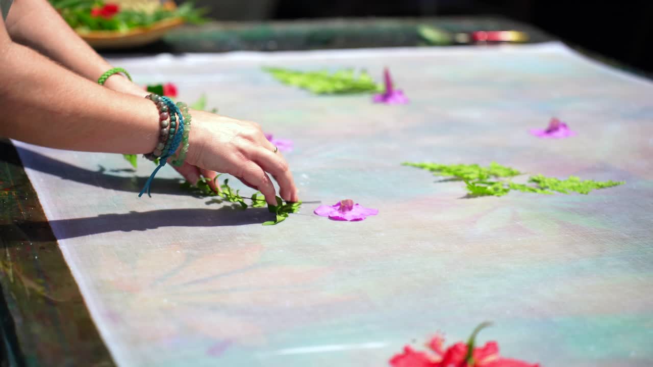 Clienti che imparano il batik fatto in casa, sarong, pareo, mentre posizionano foglie verdi e fiori su un panno bianco, Mahé, Seychelles 25fps 1
