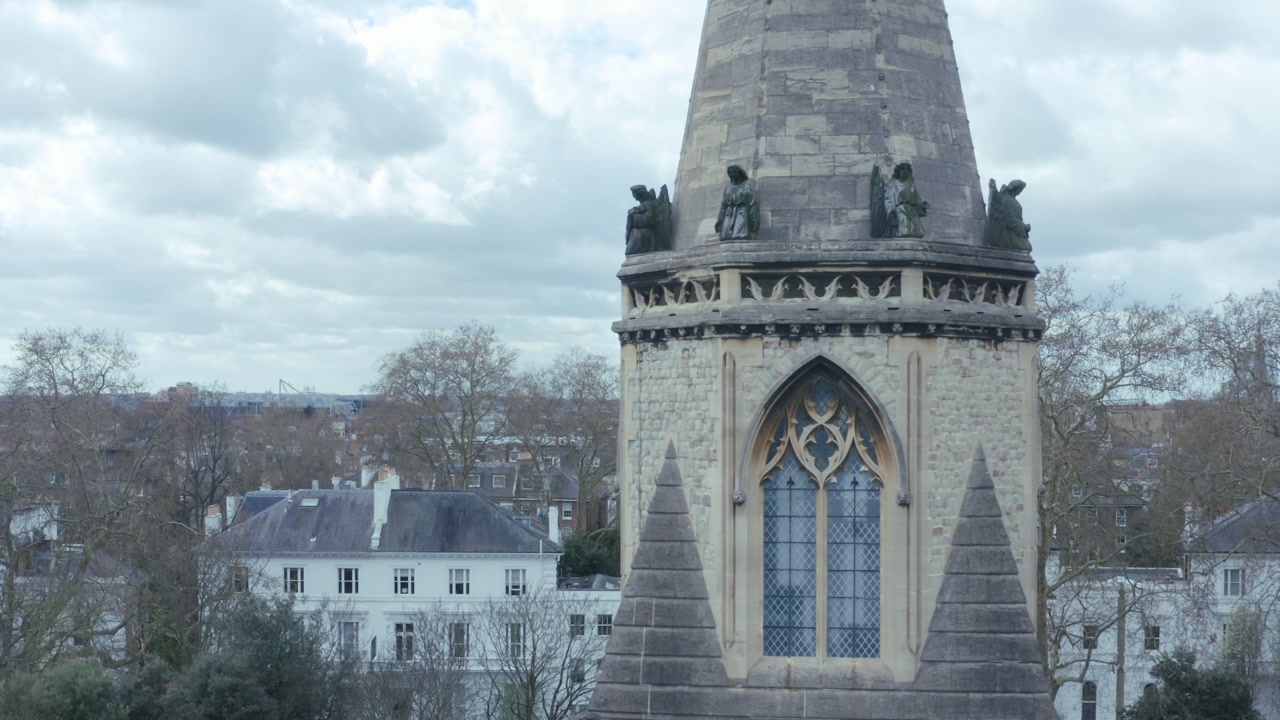 A cinematic drone shot capturing the tower of St Mary The Boltons in close detail. The shot begins with a steady lateral pan across the structure, revealing the intricate Victorian stonework, arched w
