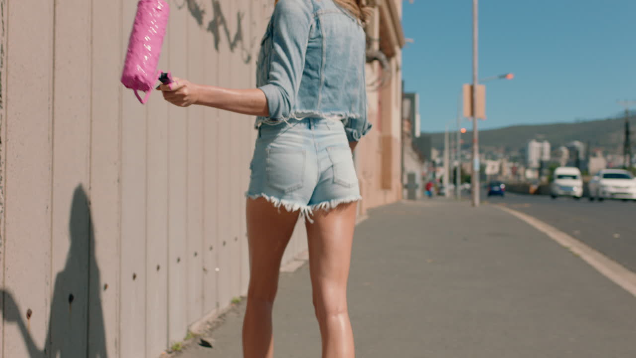 hermosa mujer artista pintando pared con pintura rosa caminando por la calle de la ciudad mujer confiada disfrutando de la expresión artística con graffiti urbano arte retro