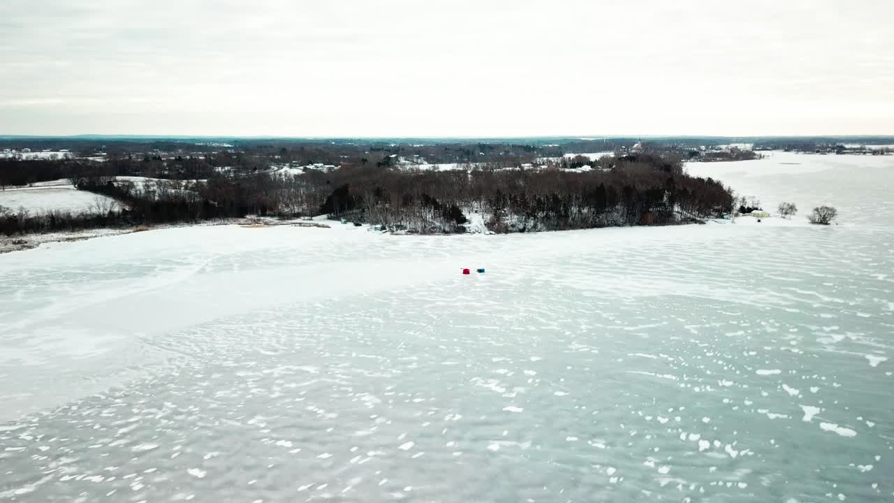 Wide to close aerial shot of an ice-fishing hut on a frozen midwestern lake. 4K