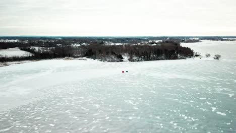 wide to close aerial shot of an ice-fishing hut on a frozen midwestern lake. 4k