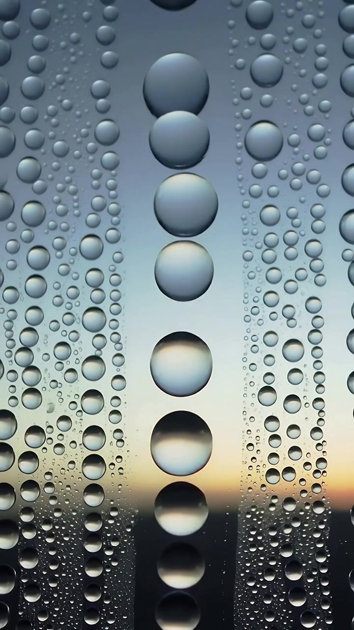Vertical video: Catching sunrise light center column big droplets reflecting horizon glow on glass
