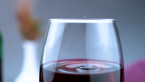 la cautivadora toma a cámara lenta muestra una sola gota de vino que desciende delicadamente en un vaso parcialmente lleno, creando un elegante espectáculo visual.