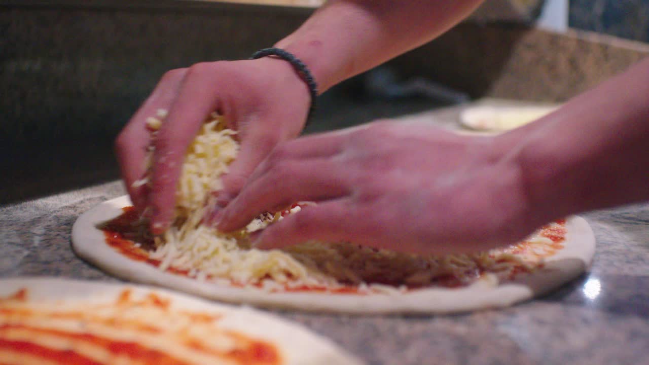 Il cuoco cosparge il formaggio grattugiato sull'impasto della pizza