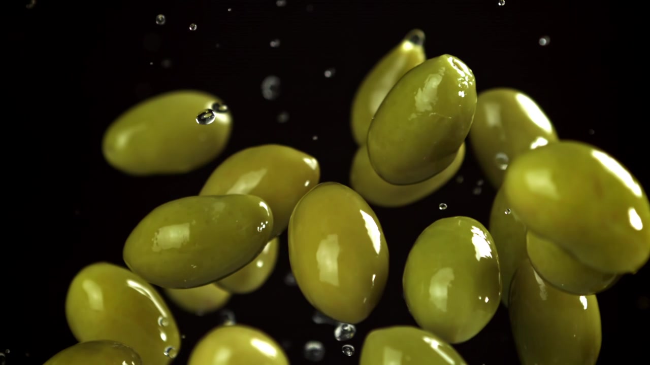 Olive verdi che cadono al rallentatore con gocce d'acqua su sfondo nero