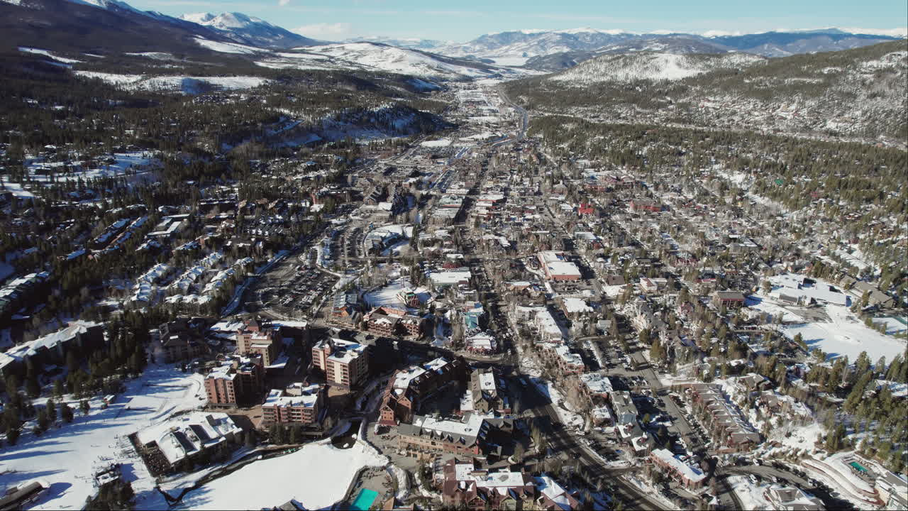 A wide rising aerial of beautiful snow-covered Breckenridge, as cars carrying skis and snowboards drive into the popular Colorado mountain town for a ski vacation at the world famous resort.