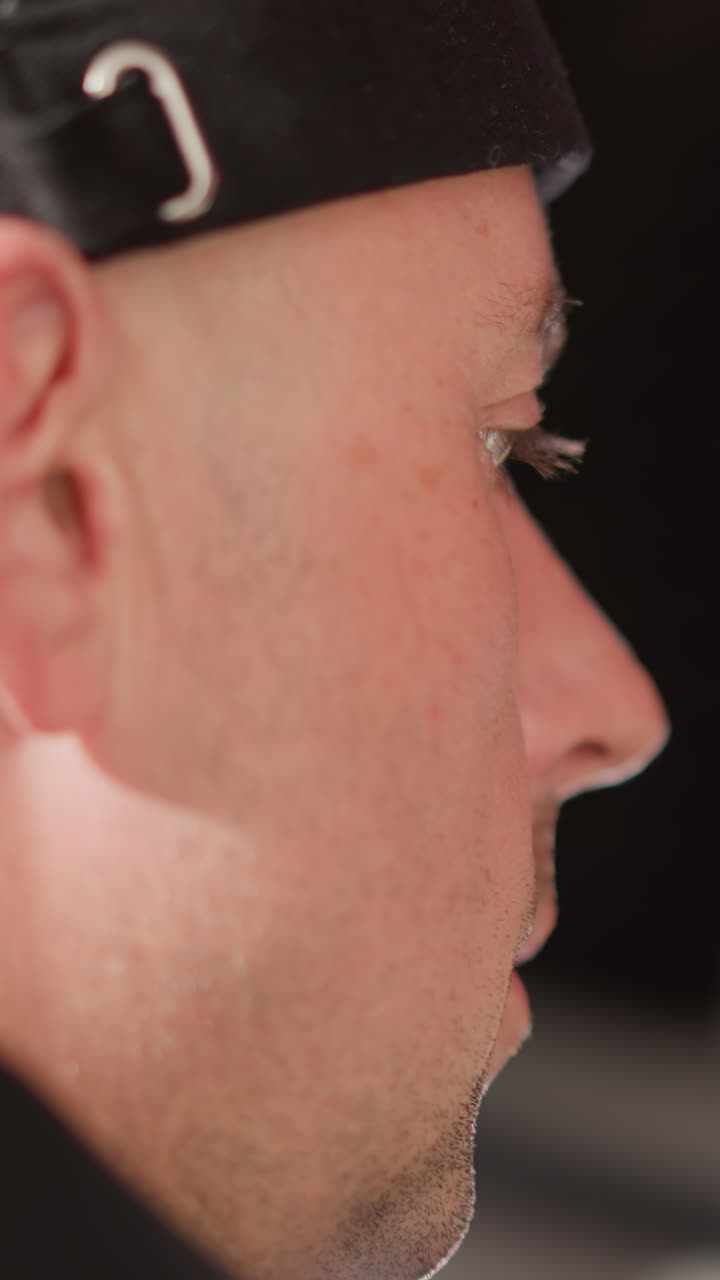 primer plano de la cara de un hombre con una gorra negra, con una expresión enfocada. en el fondo borroso, un altavoz es visible, lo que indica un estudio o un entorno de producción de audio